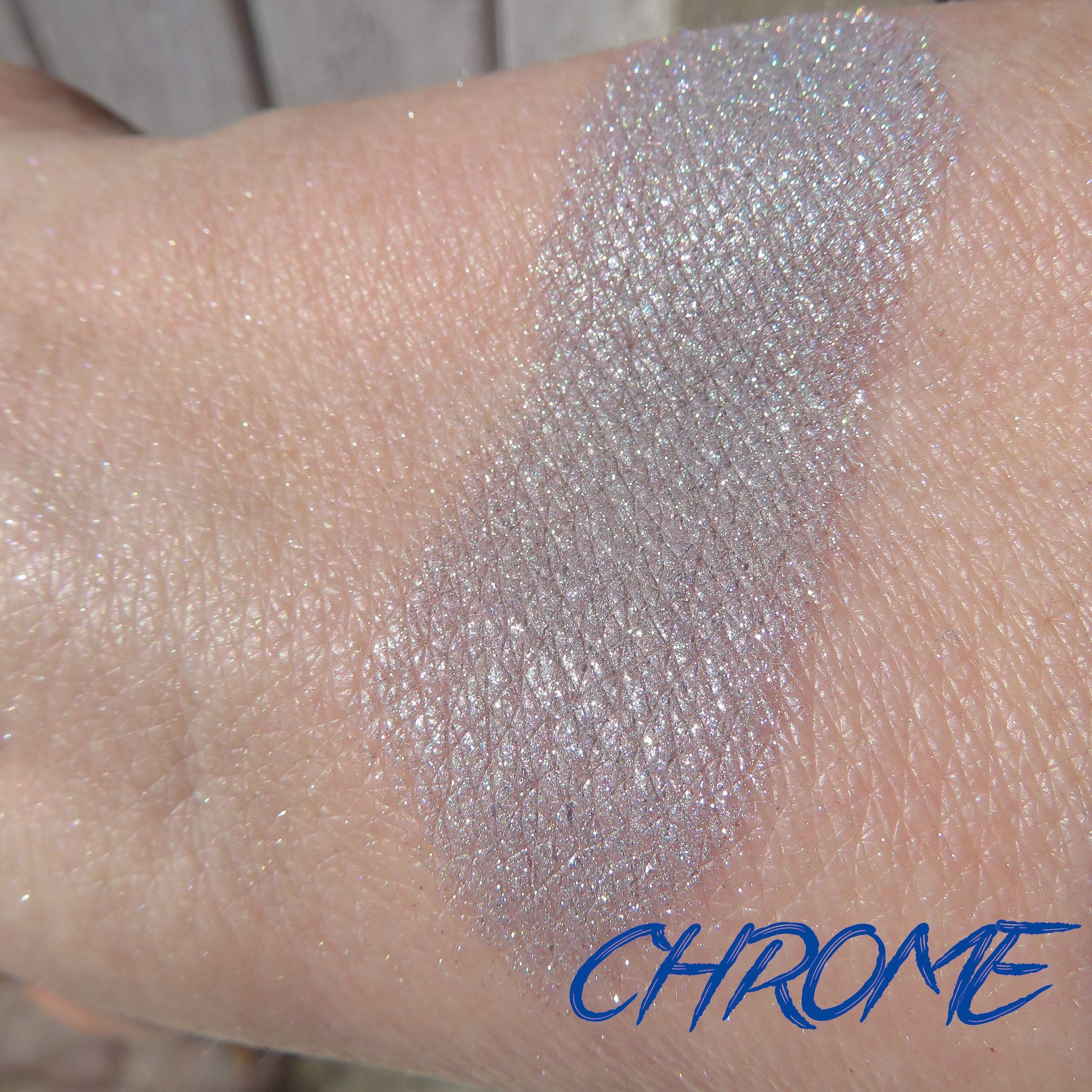 Side view of shimmery silver chrome loose pigment eyeshadow in a clear jar with black lid, showcasing fine metallic particles.
