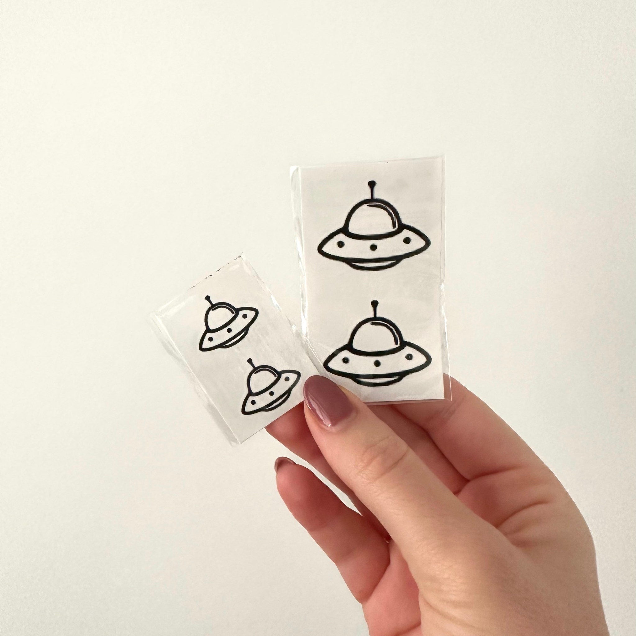 Close-up of skin-safe temporary tattoo UFO set showing intricate metallic designs on protective backing paper