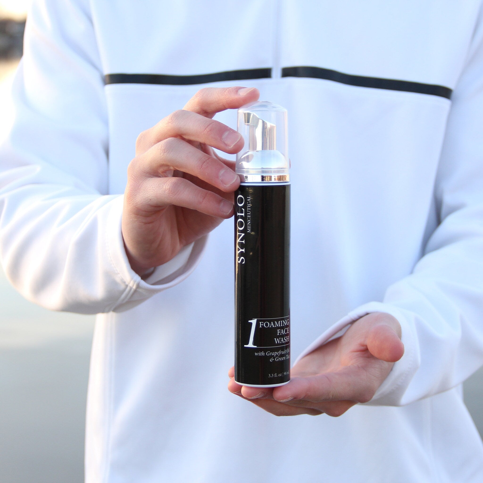 Foaming face wash bottle, black and silver, held in hands, SYNOLO brand visible