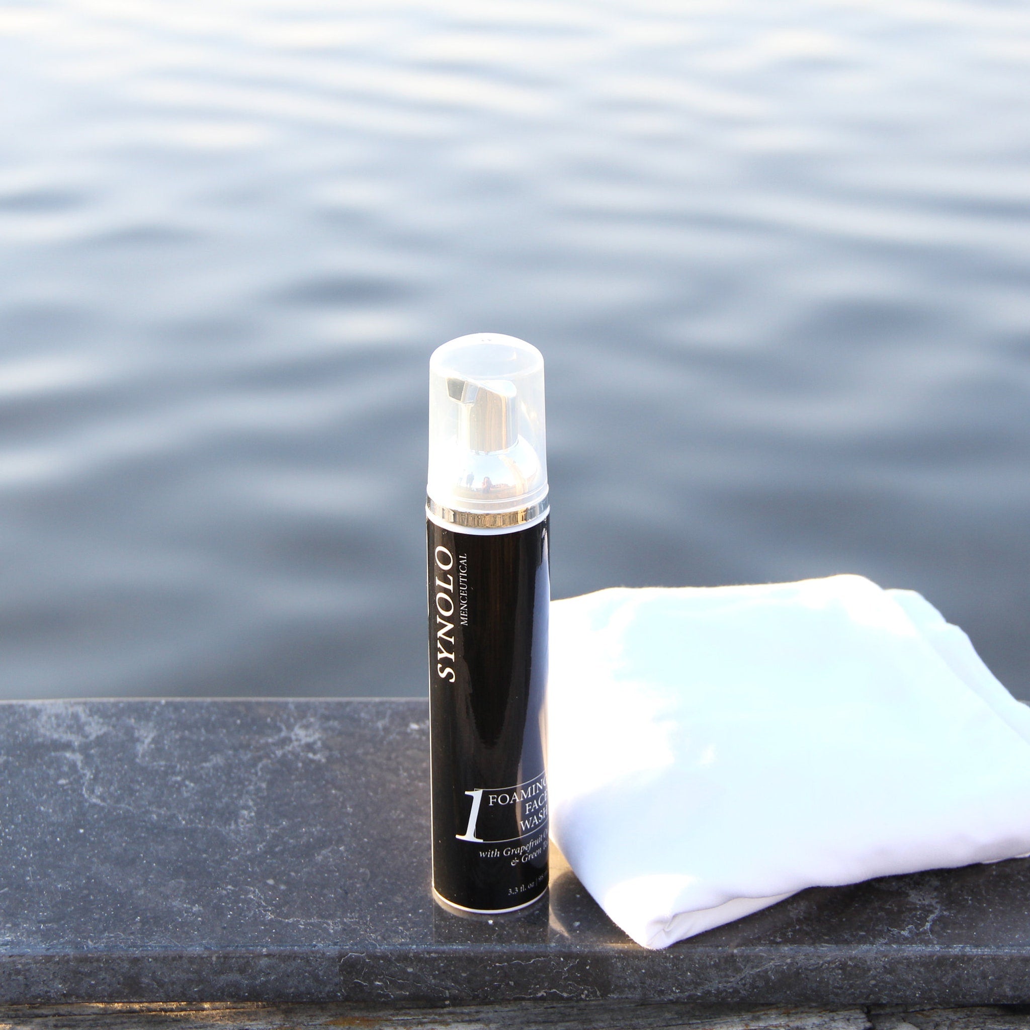 Foaming face wash bottle with black and silver design, white cloth on a dark surface