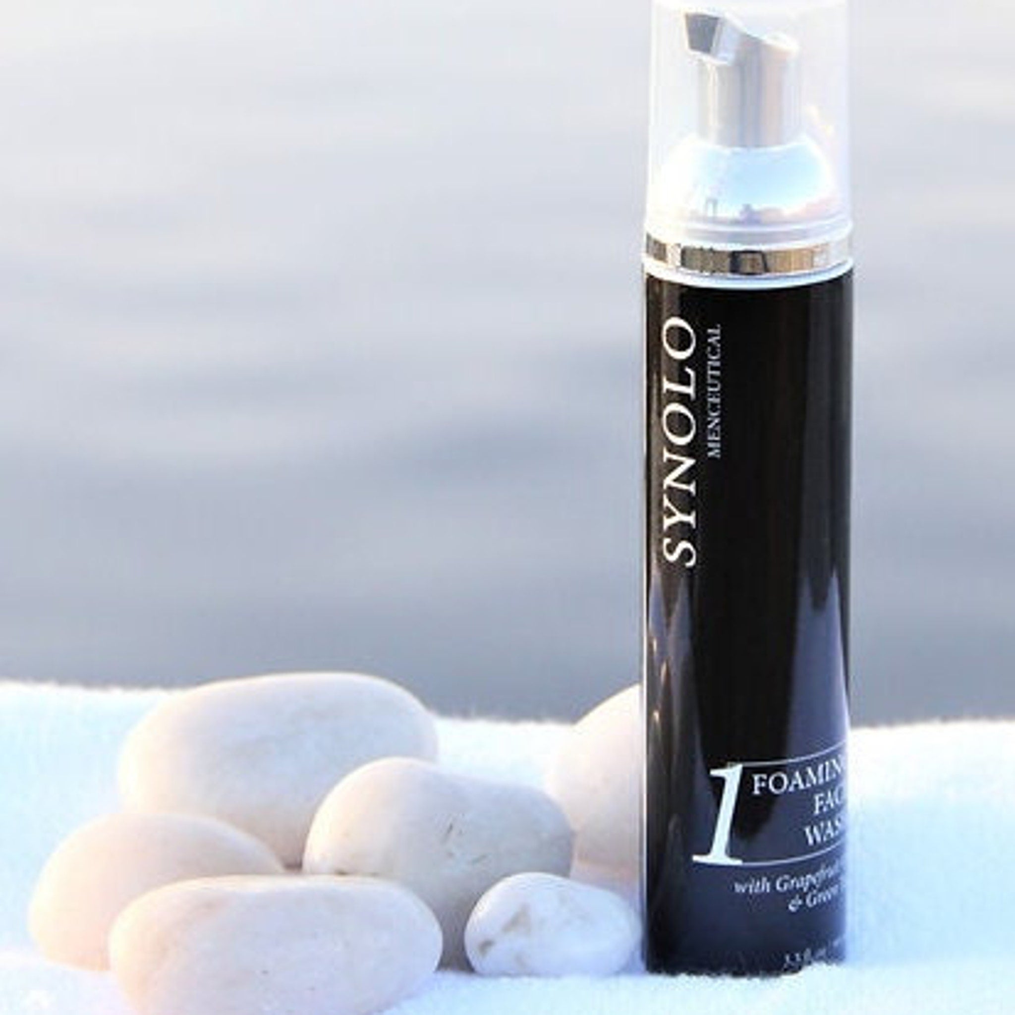 Foaming face wash bottle, black and silver, with "SYNOLO" branding and white label, on white surface