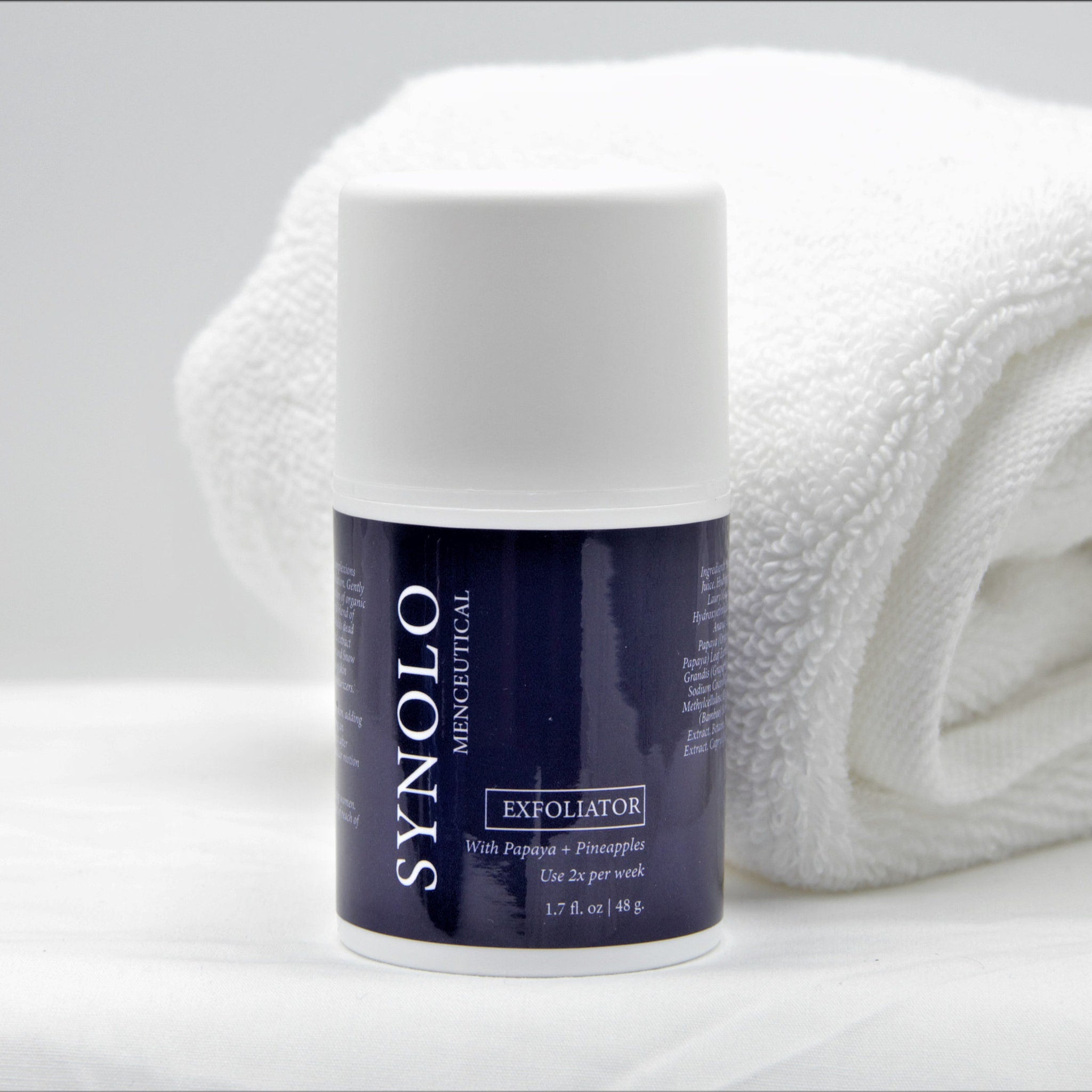Exfoliator bottle with white and navy label, white towel in background, SYNOLO brand visible.