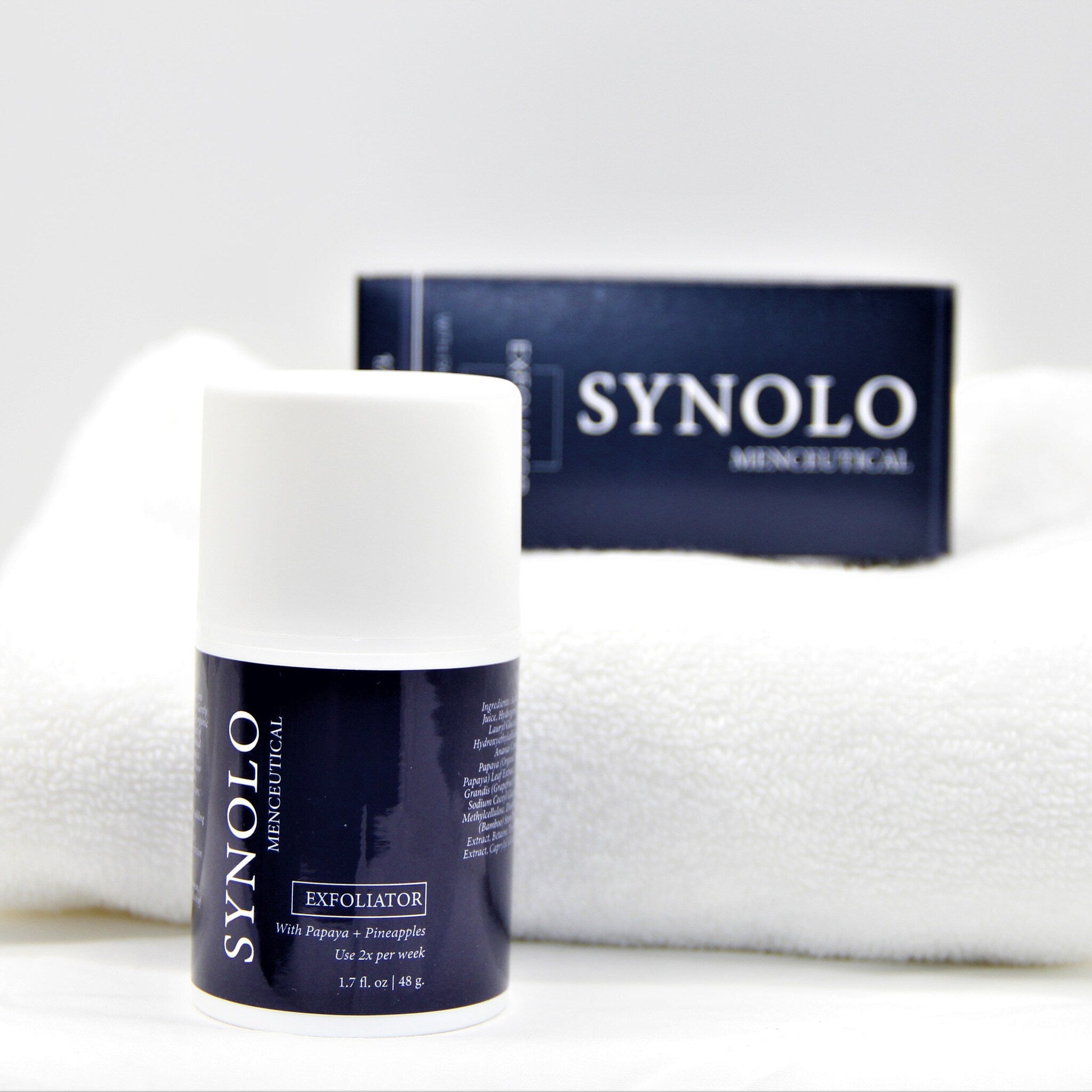 Exfoliator product with white and navy blue cylindrical bottle, SYNOLO brand text visible, on white towel