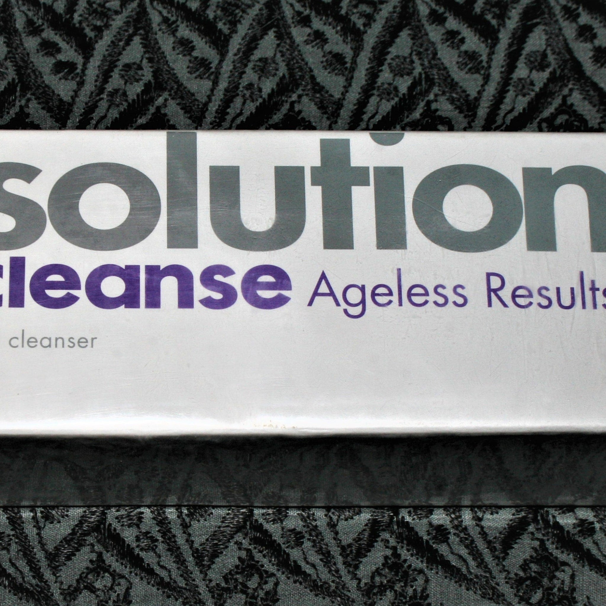 Solution cleanser box with white, purple, and gray text on patterned background