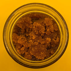 Brown granular substance in a clear glass jar with a yellow background