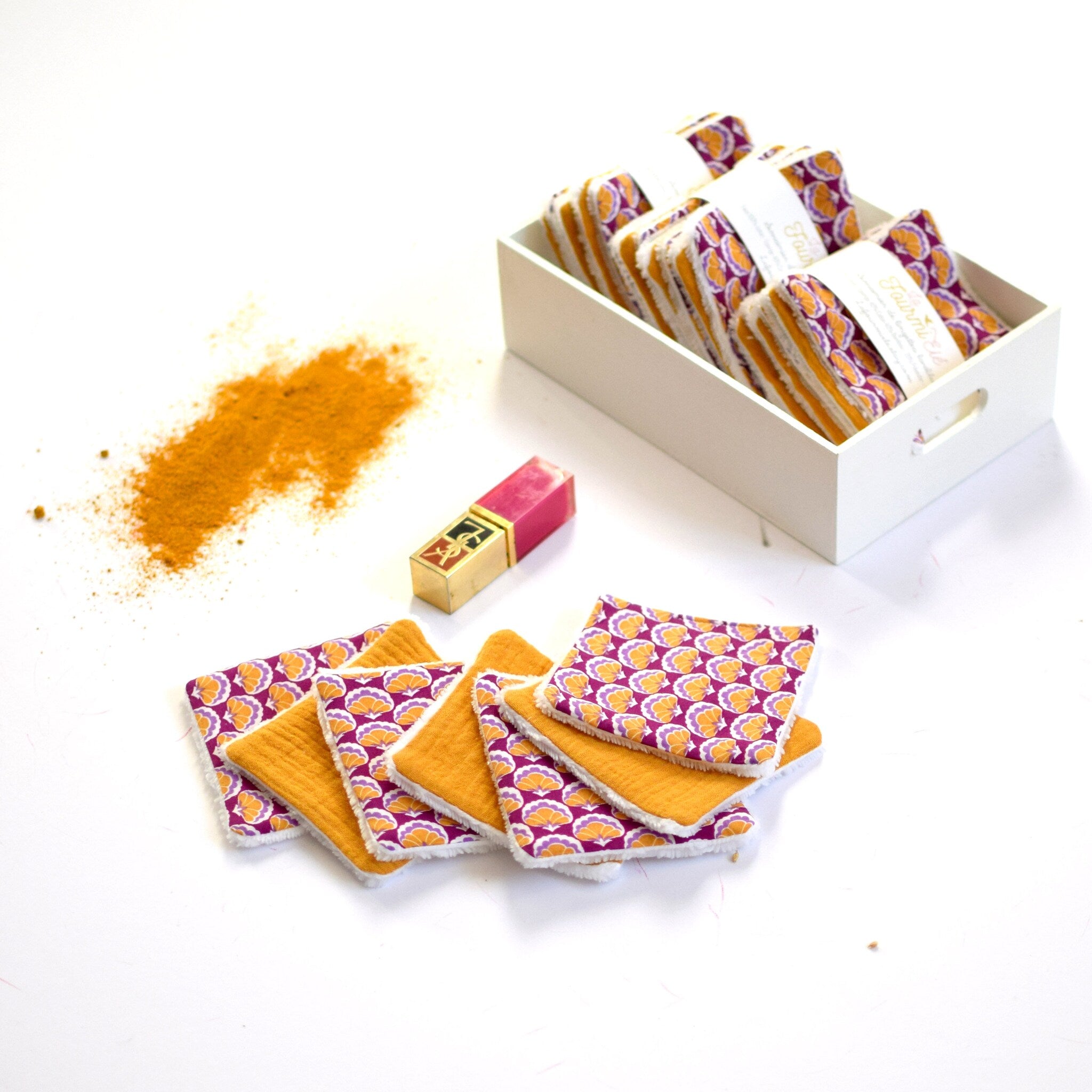 Reusable face pads with orange and purple floral pattern, yellow textured fabric, white trim, and a lipstick beside them