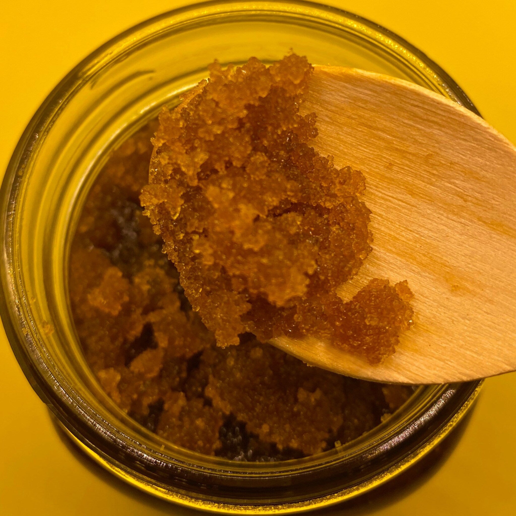 Brown sugar scrub with brown granules in a glass jar with a wooden spoon