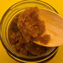Brown sugar scrub with brown granules in a glass jar with a wooden spoon