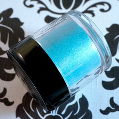 Swatch of iridescent teal and purple loose eye shadow with shimmer on fingertip against neutral background