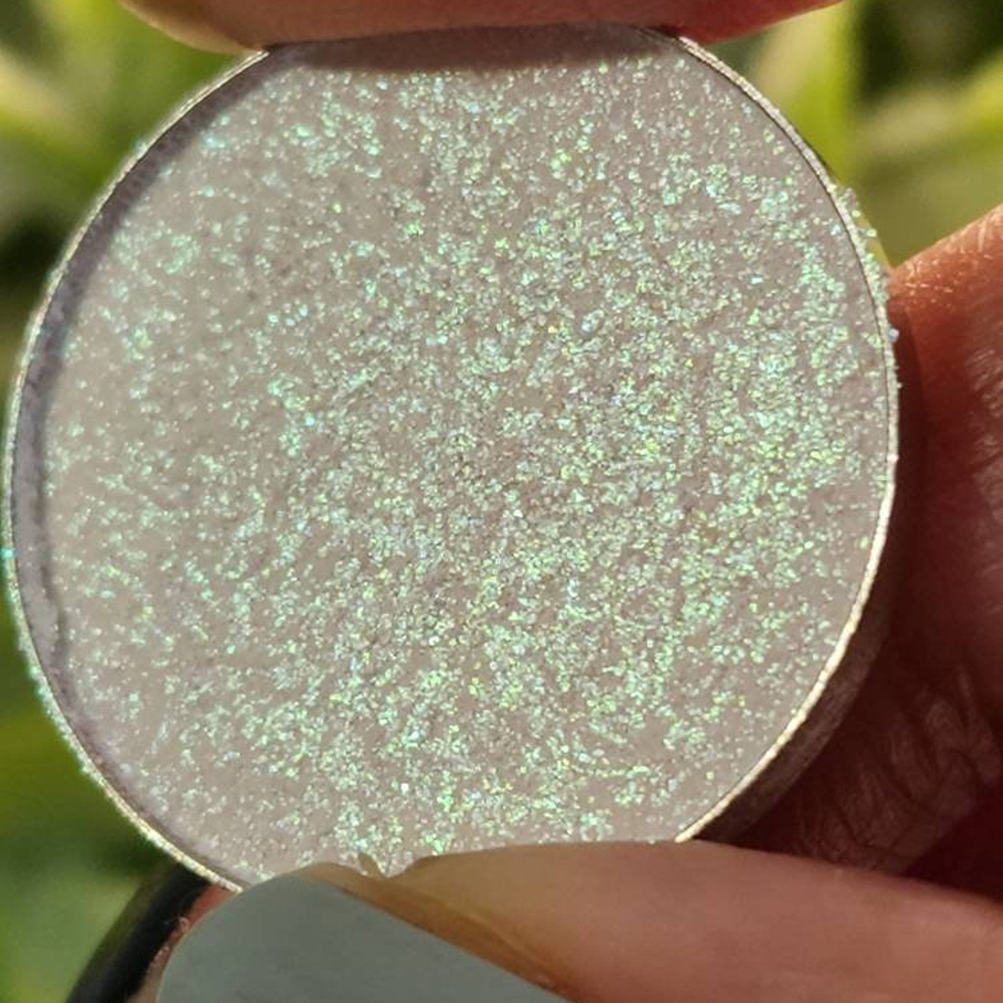 Sea Witch eyeshadow pan in neon green and pink duo chrome shimmer, displayed on sleek black packaging