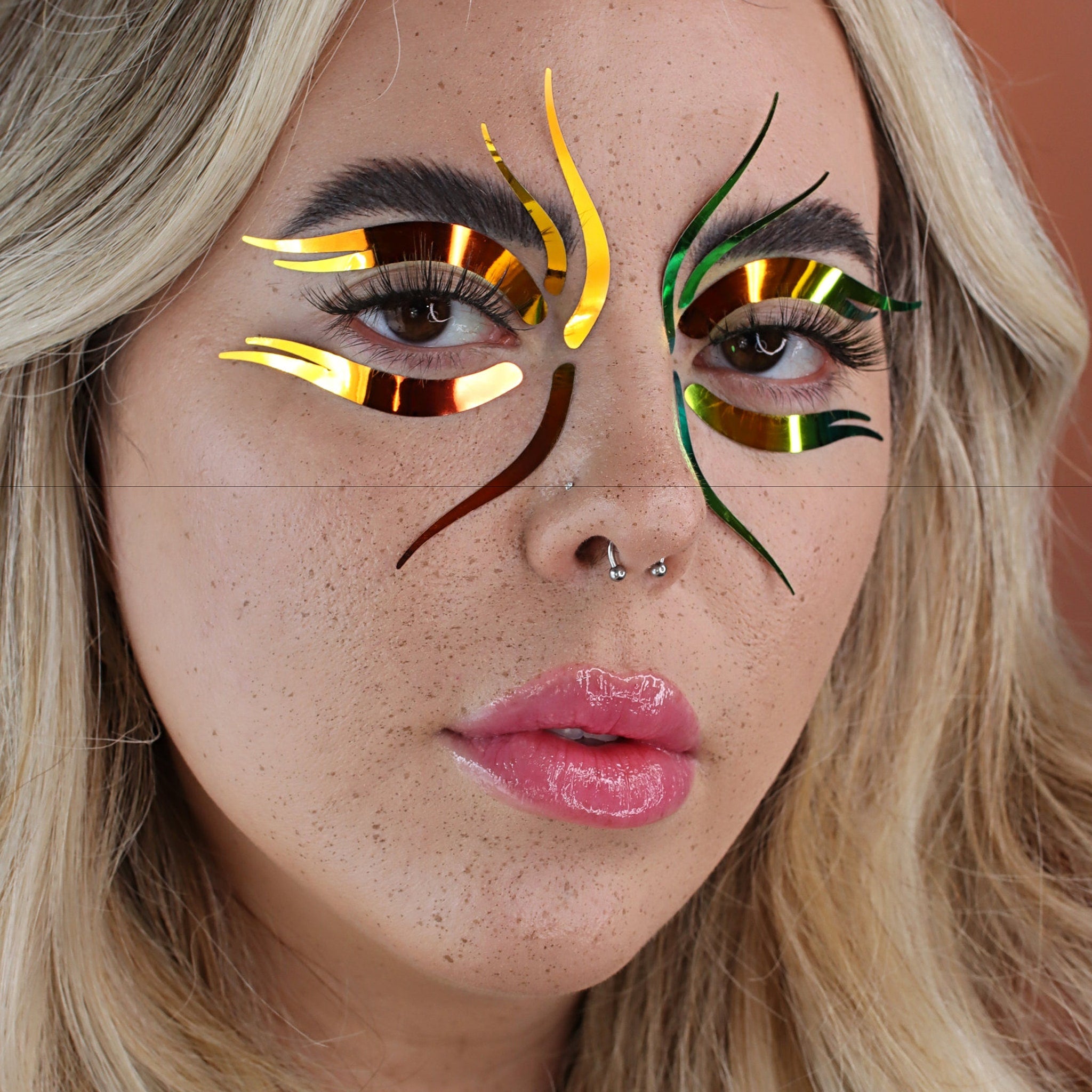 Eye makeup stickers with gold and green metallic accents on a face of a woman with blonde hair