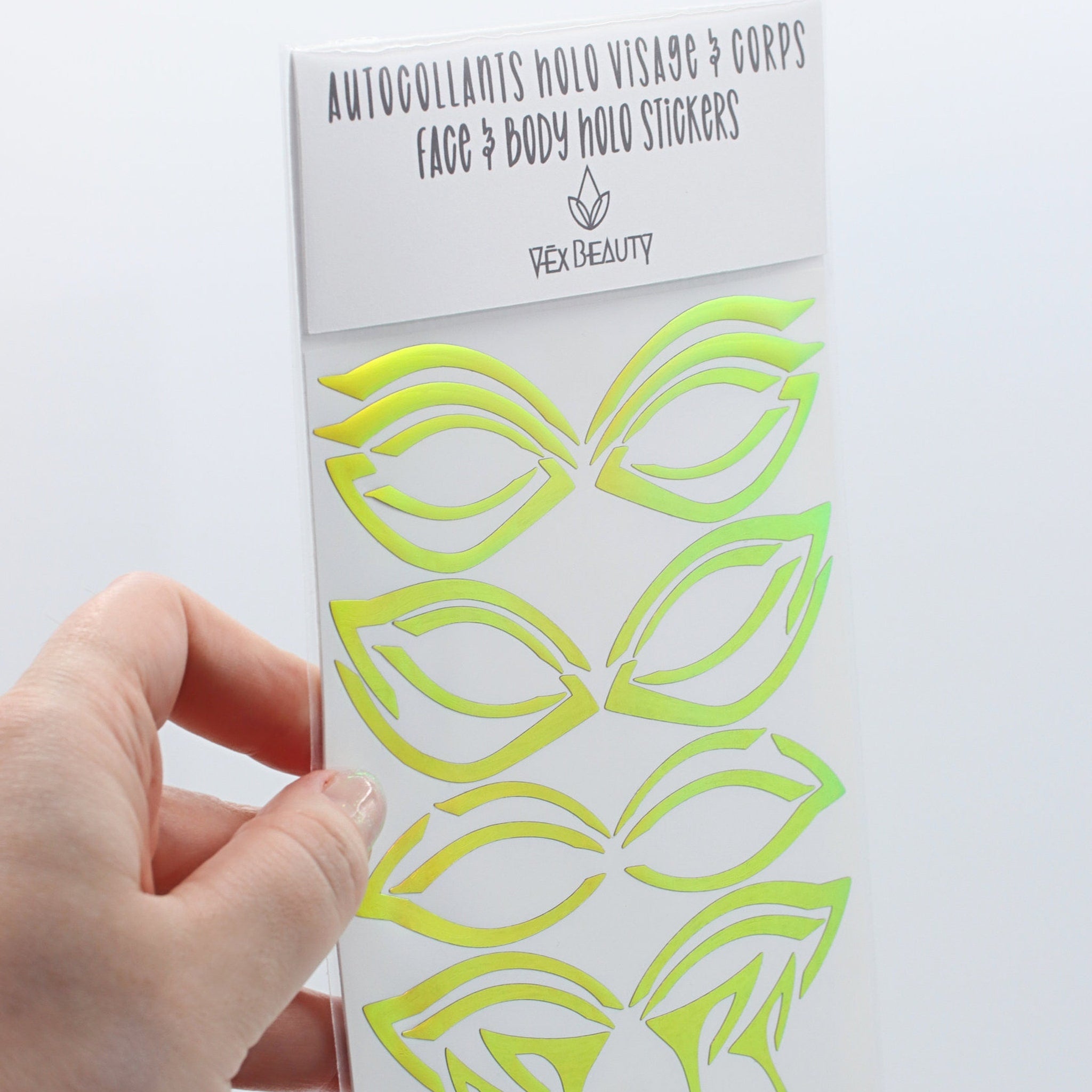 Face and body stickers with green and yellow holographic design, Vex Beauty brand packaging held by hand
