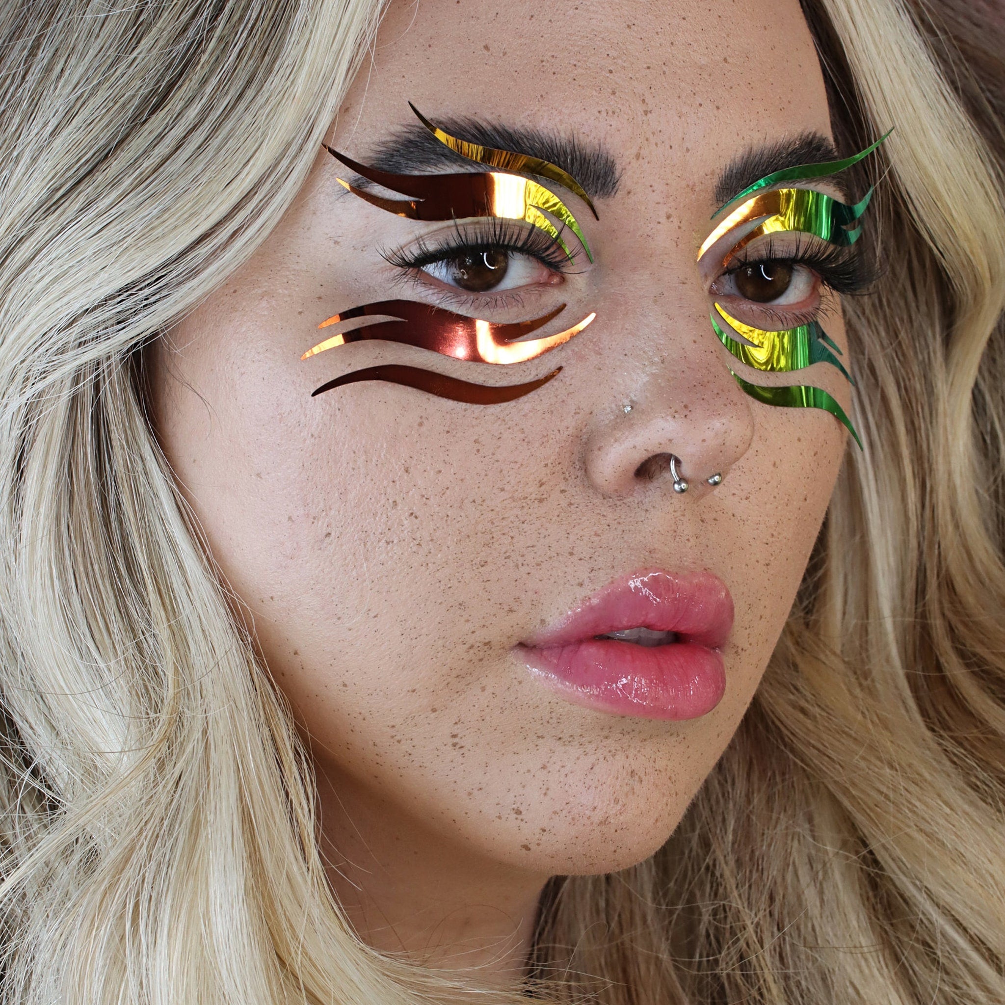 Eye makeup with metallic gold and green accents, applied on face with blonde hair