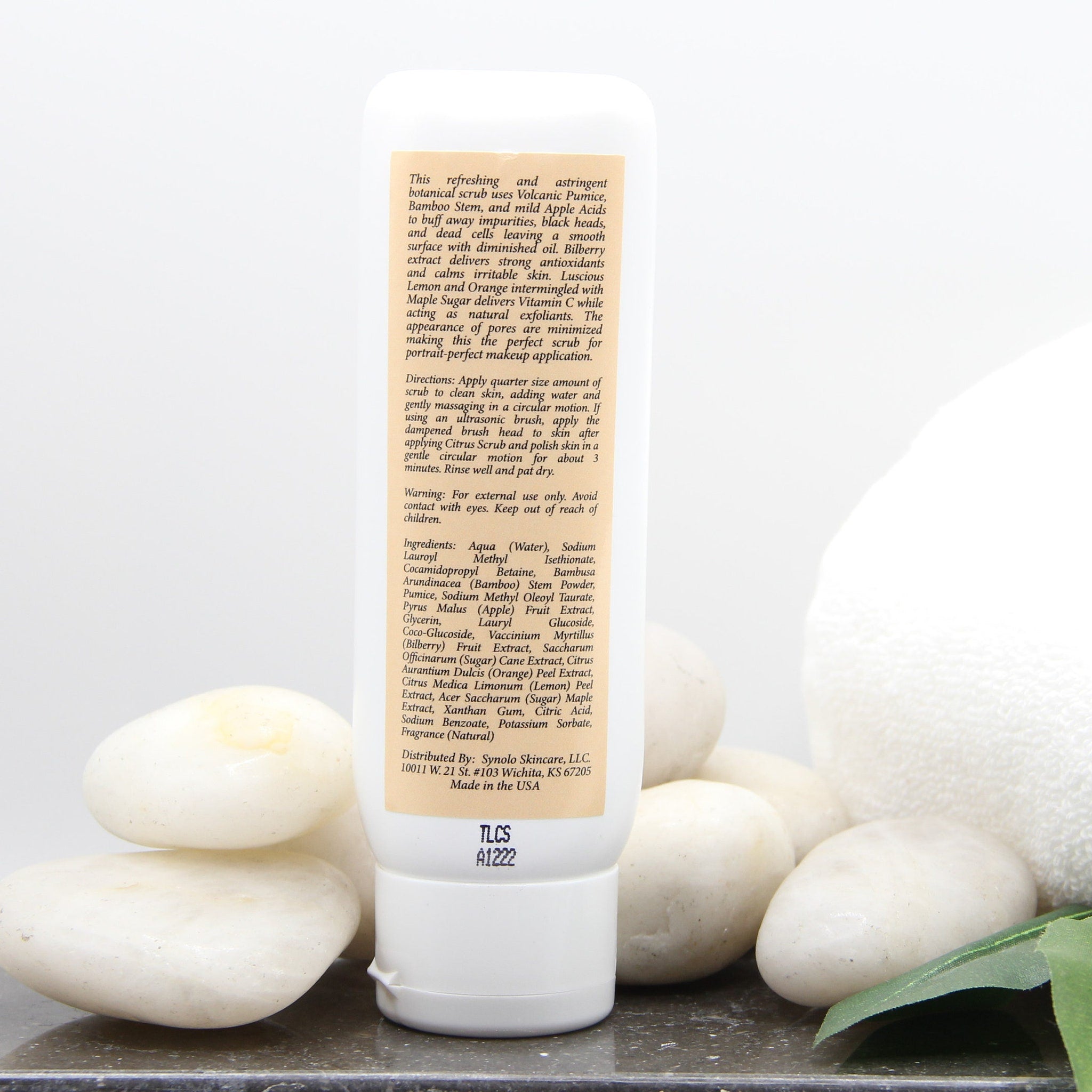 White skincare product bottle with white cap and text on label, on white rocks