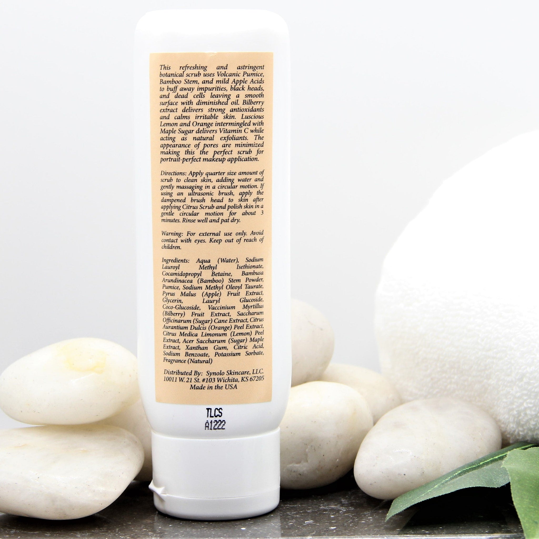 Facial scrub bottle, white plastic, beige label, with white stones in background