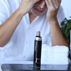 Facial cleanser bottle with black and silver design, white foam on face, and white shirt visible