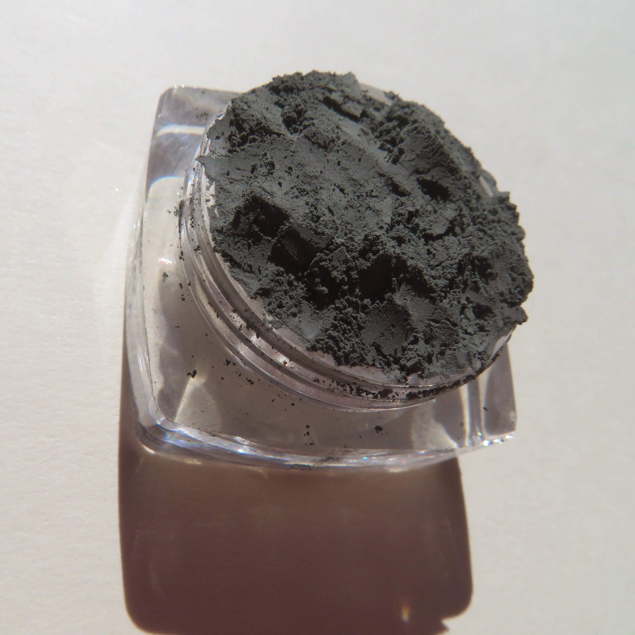Side view of dark matte green tea mineral eyeshadow in loose powder form with vegan label visible