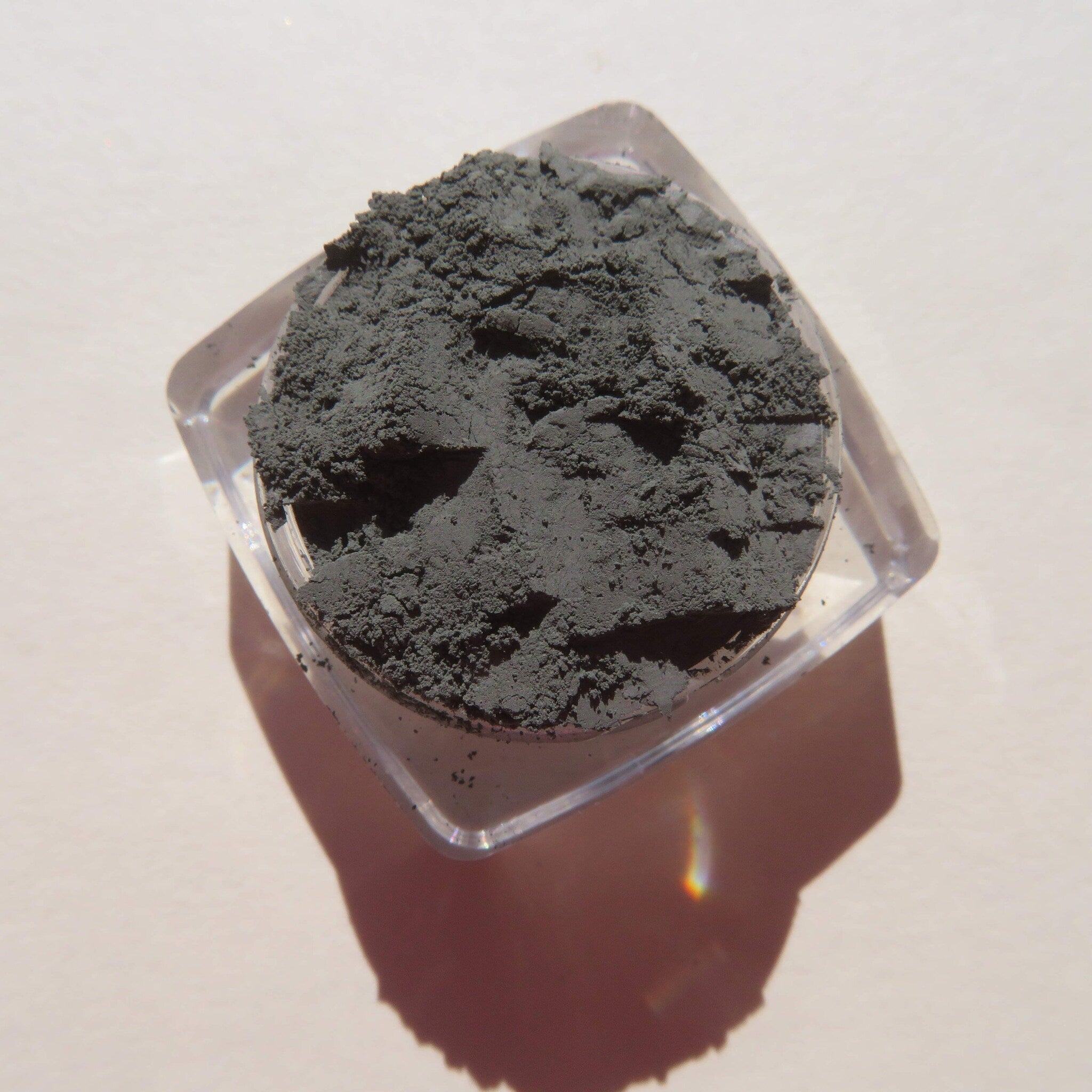 Side view of loose dark matte green tea mineral eyeshadow powder spilling from jar onto surface