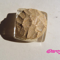 Eyeshadow pigment, golden shimmer, textured powder, in clear jar, Darcy logo visible
