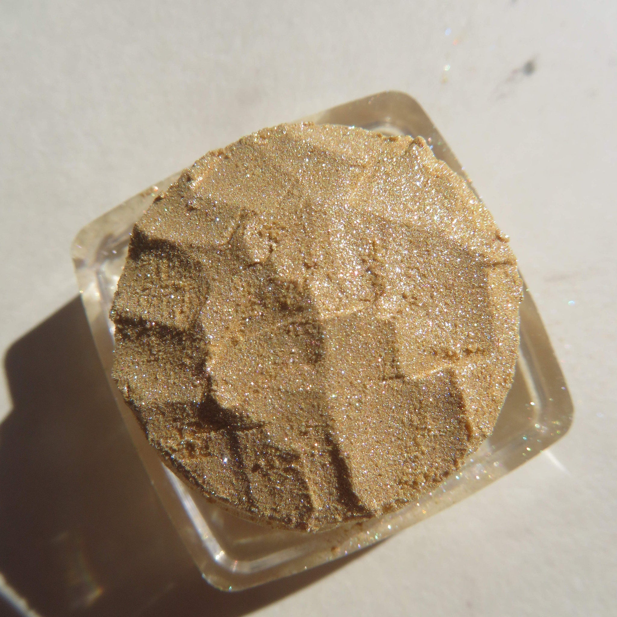 Glitter eyeshadow, gold shimmer, textured powder, in clear square container