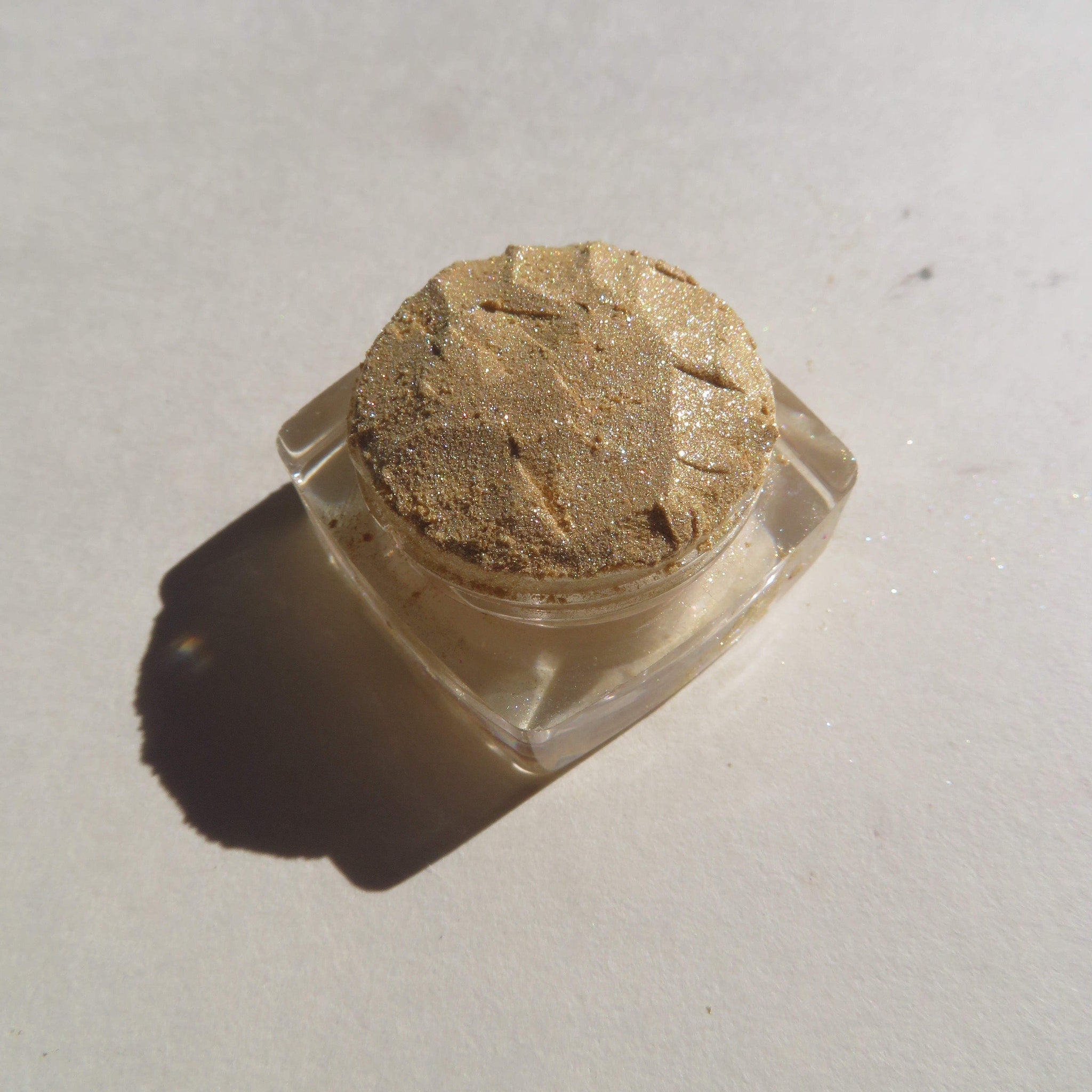Glitter eyeshadow pot with gold color, clear container, and textured surface
