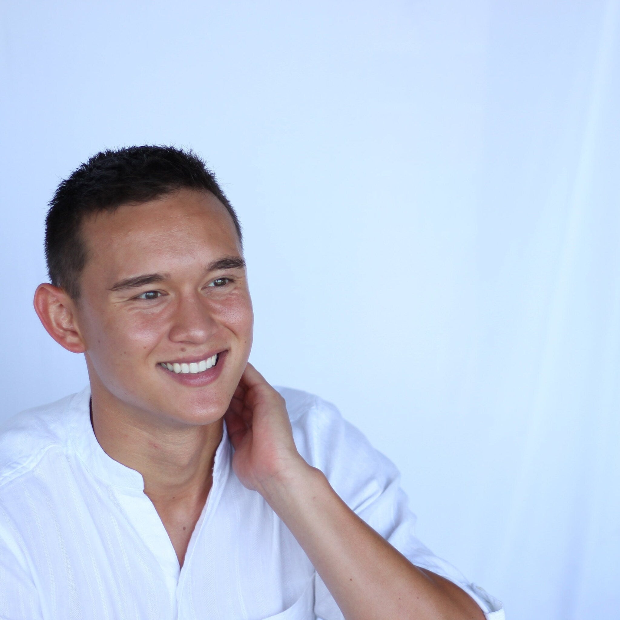 Man smiling with short dark hair wearing white collared shirt, hand on neck