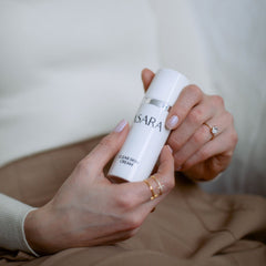 Clear skin cream bottle, white and silver, held in hands with rings