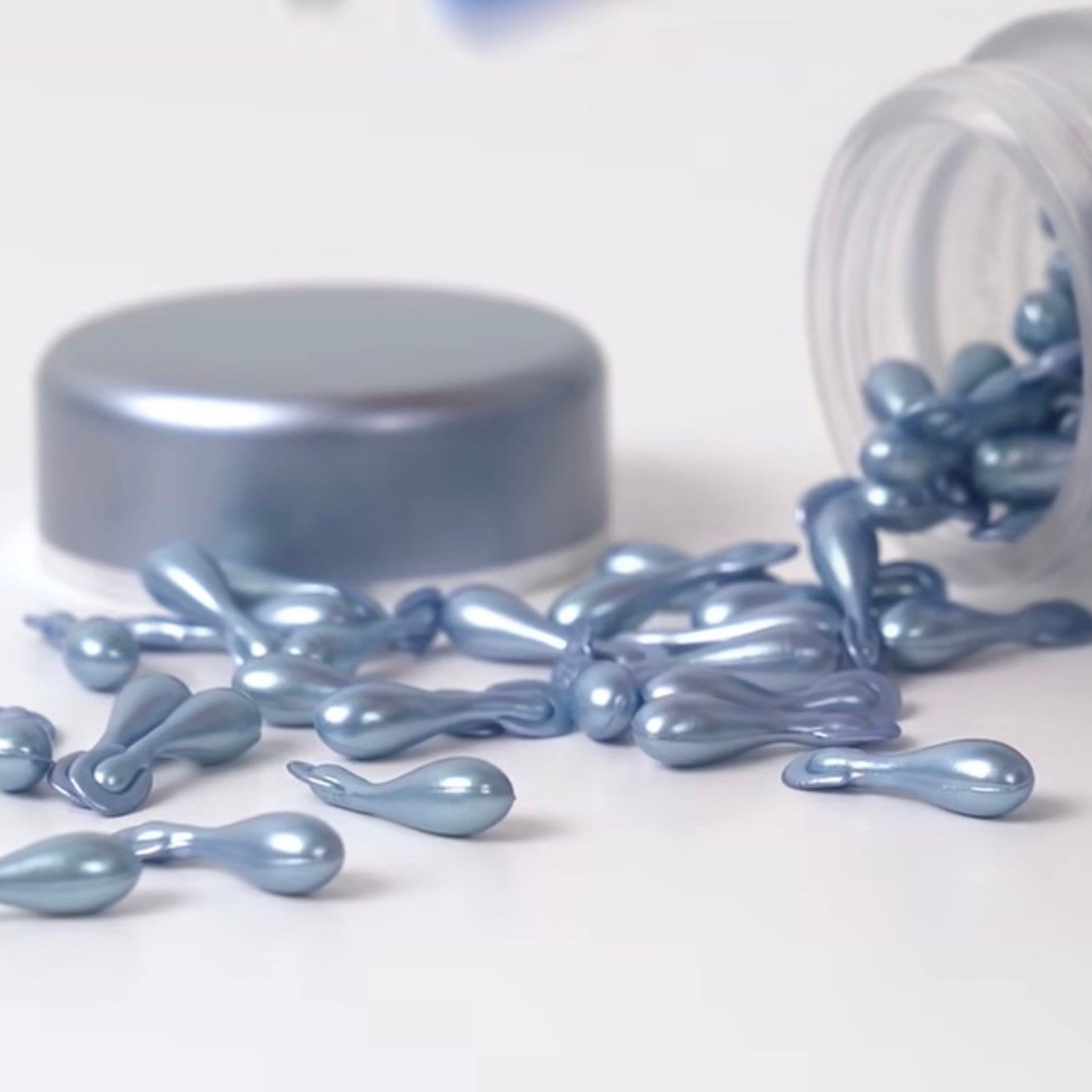 Capsules, pearlescent blue, teardrop shaped, scattered on white surface