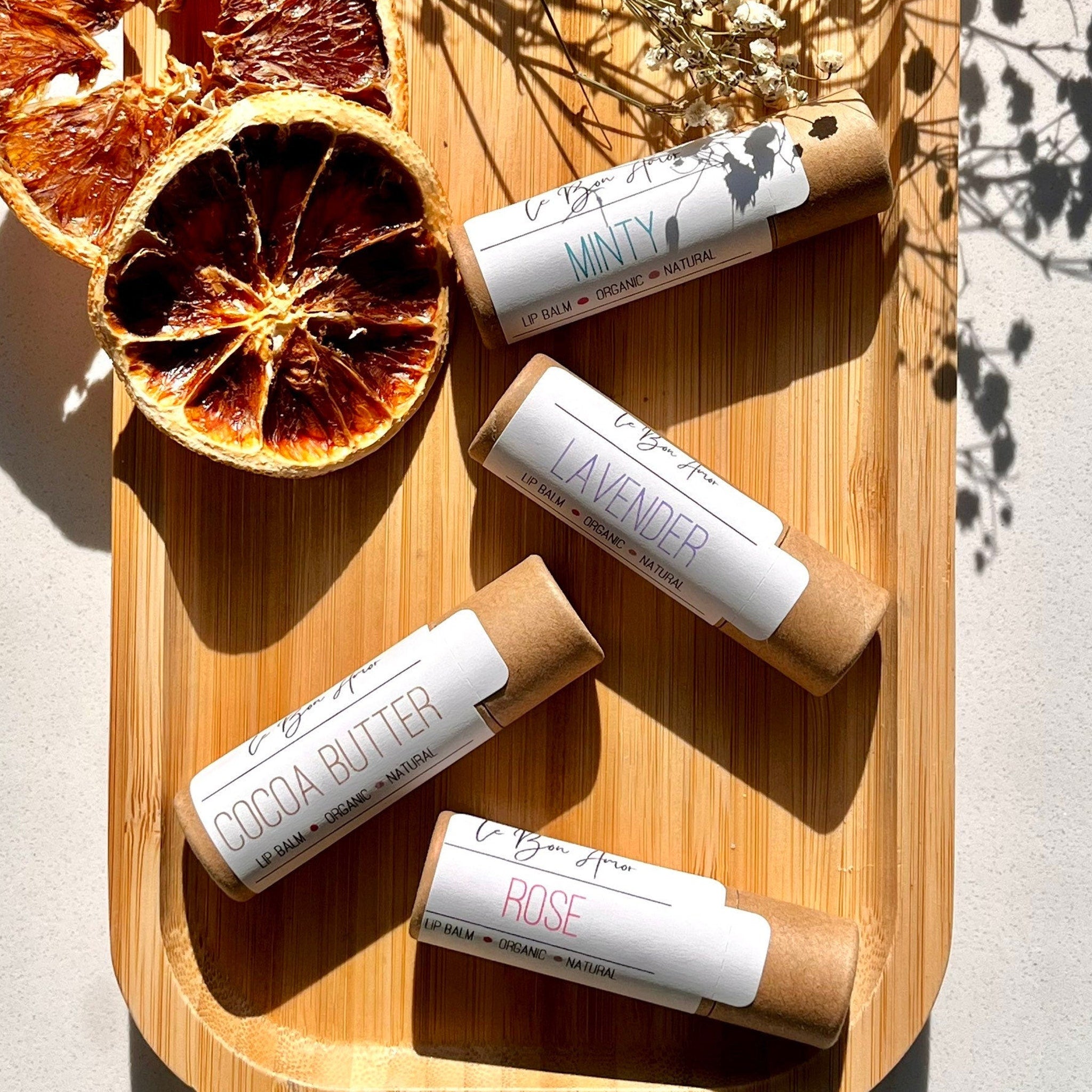 Lip balm tubes with white labels, brown paper tubes, on a wooden tray with dried orange slices