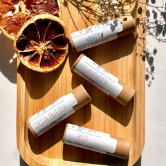 Lip balm tubes with white labels, brown paper tubes, on a wooden tray with dried orange slices