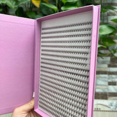 Eyelash extensions in a pink box, black lashes, and white backing, ready for use.