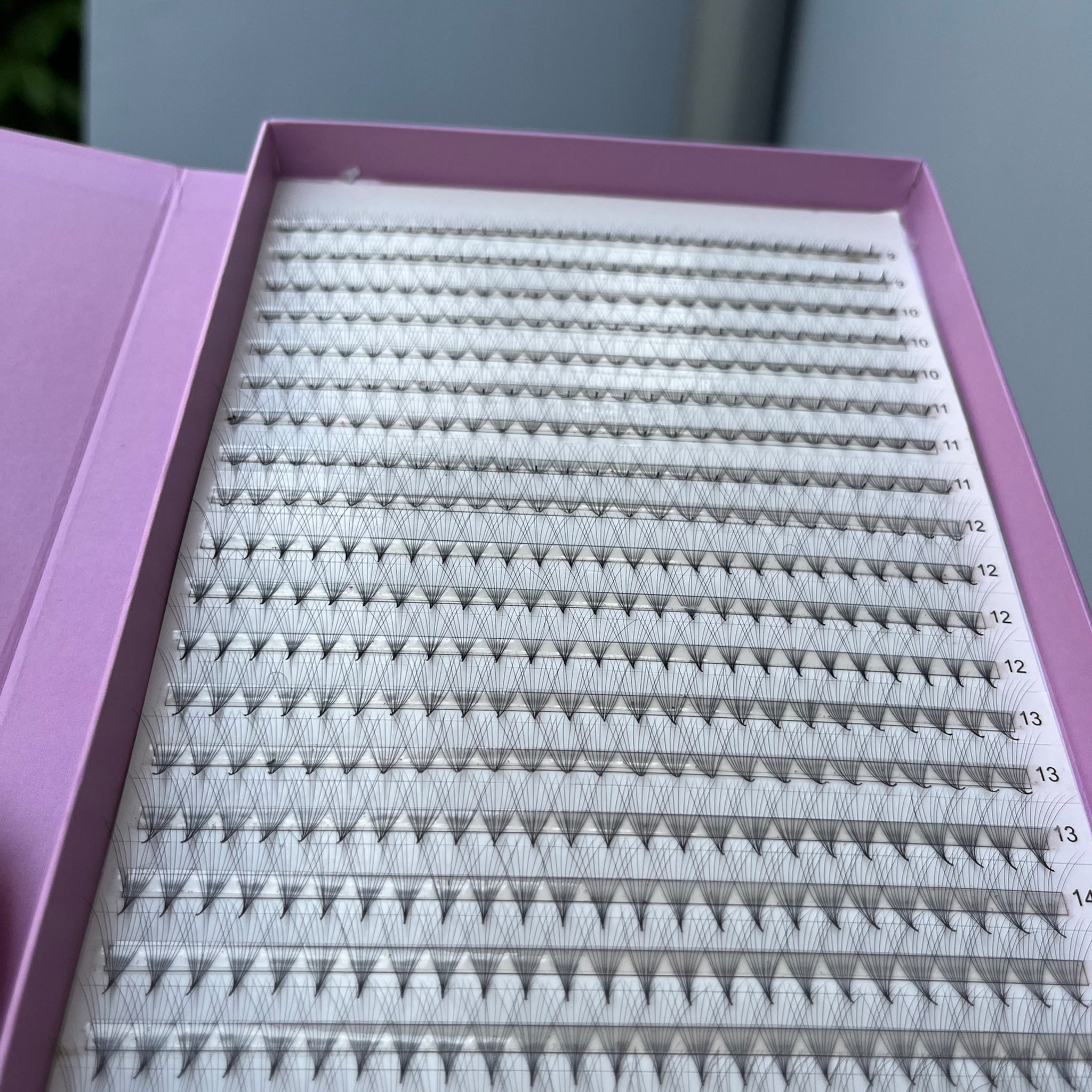 Eyelash extensions in a purple case with black lashes and white backing, organized by length