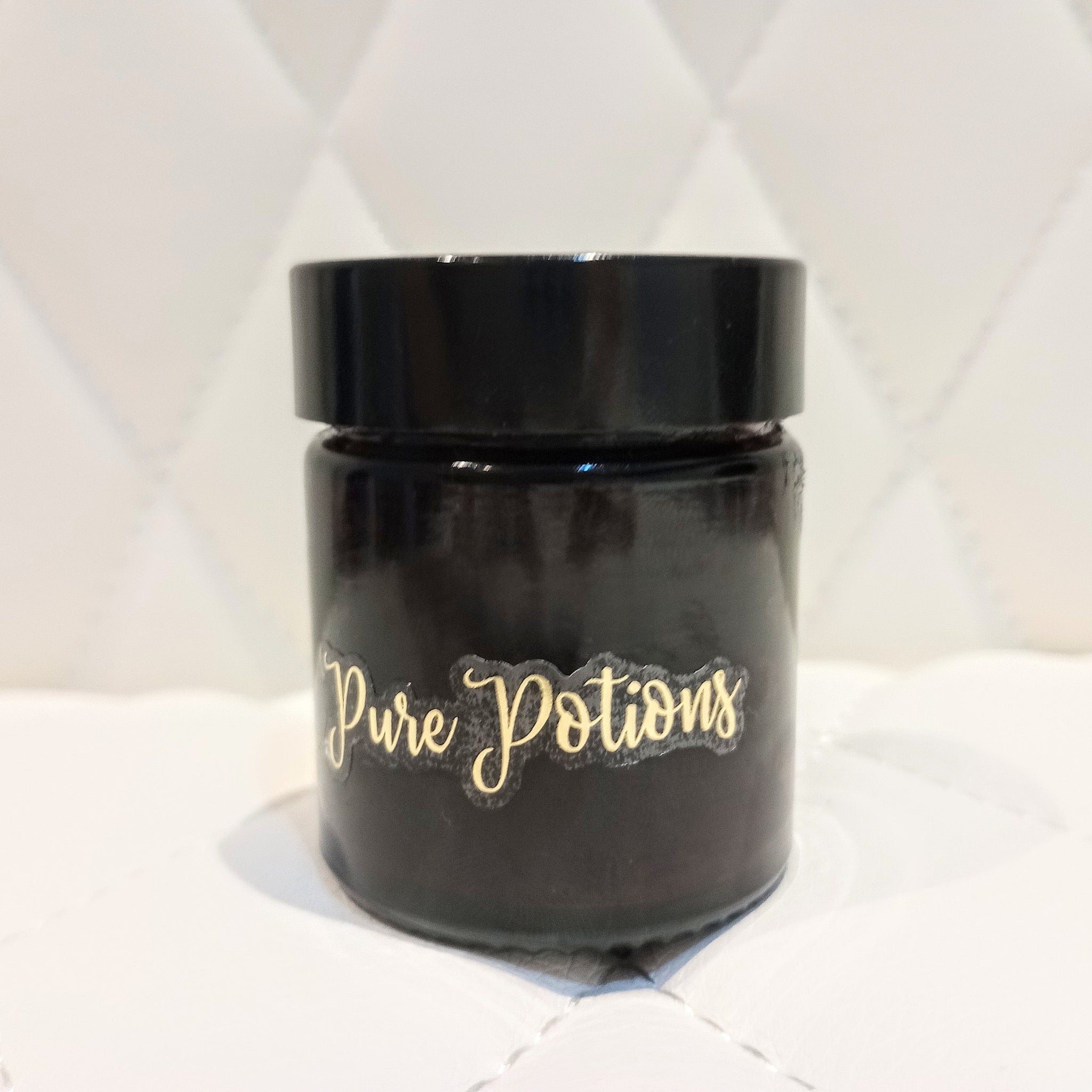 Jar with black glass, black lid, and gold "Pure Potions" label on white background.