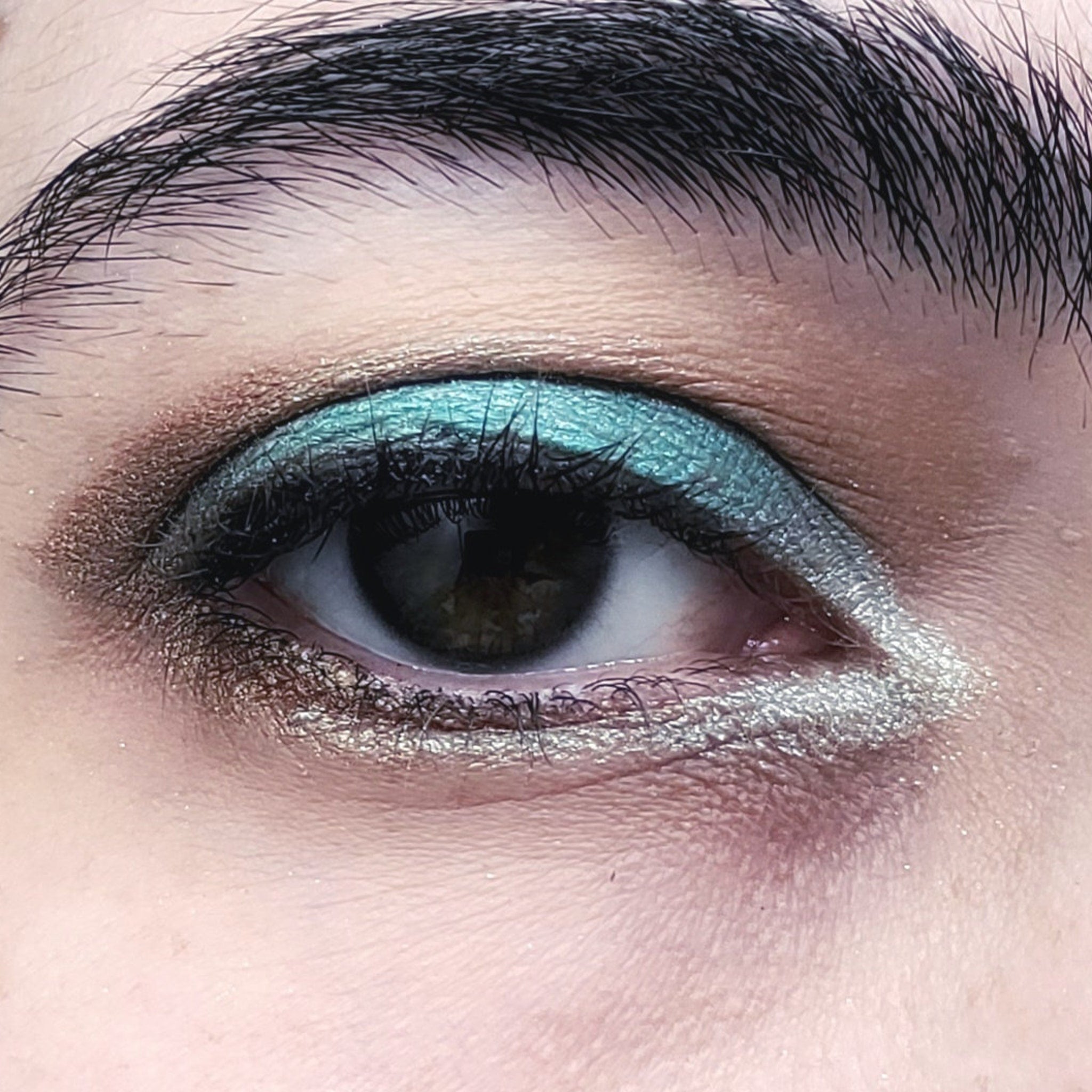 Close-up of a hand applying shimmery teal eye shadow with a blending brush for a smoky eye effect