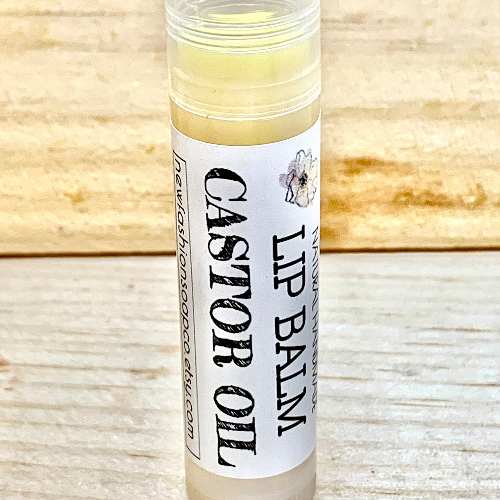 Lip balm tube with white label, black text, and floral design on a wood background