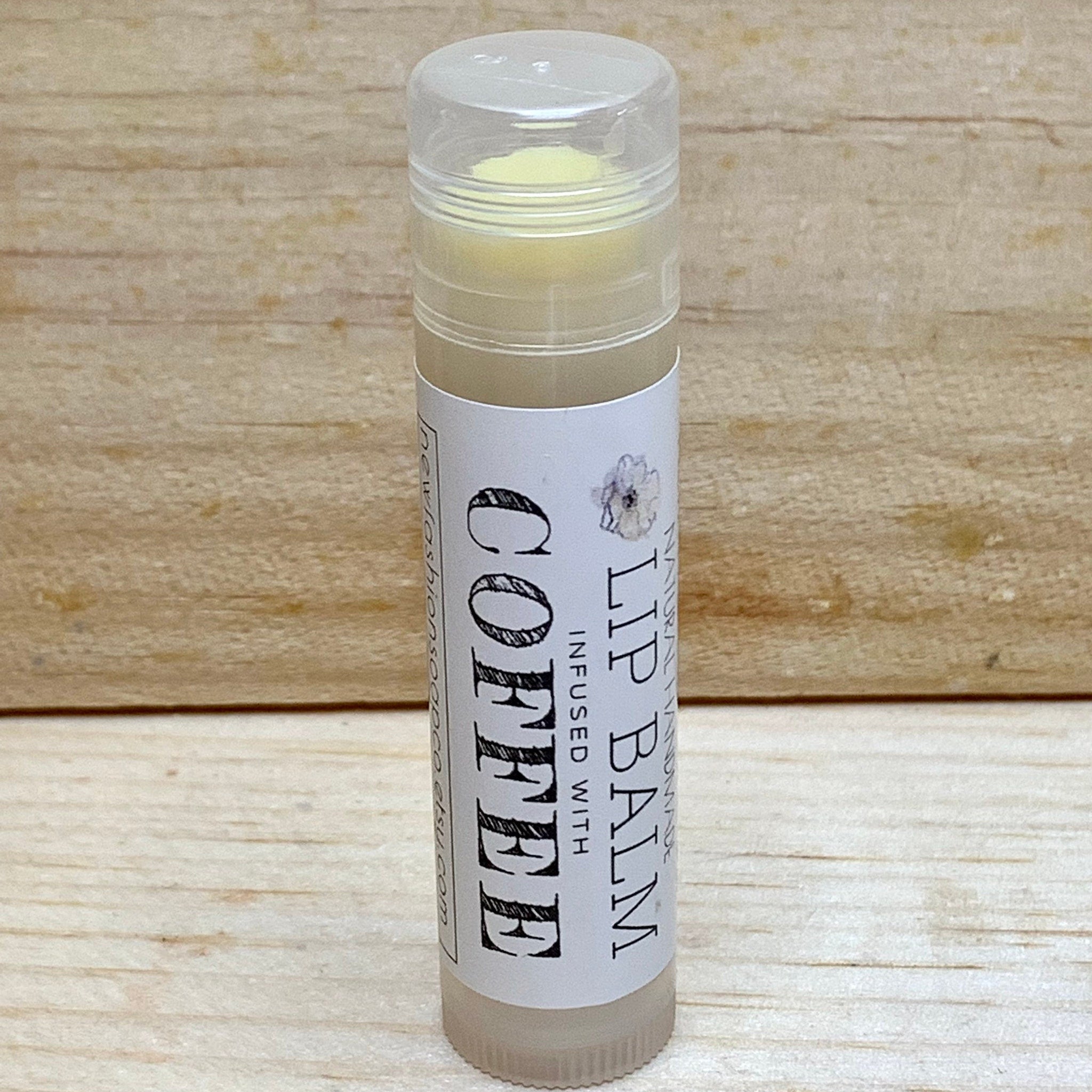 Lip balm tube with clear plastic cap, white label, and coffee text, on wood background