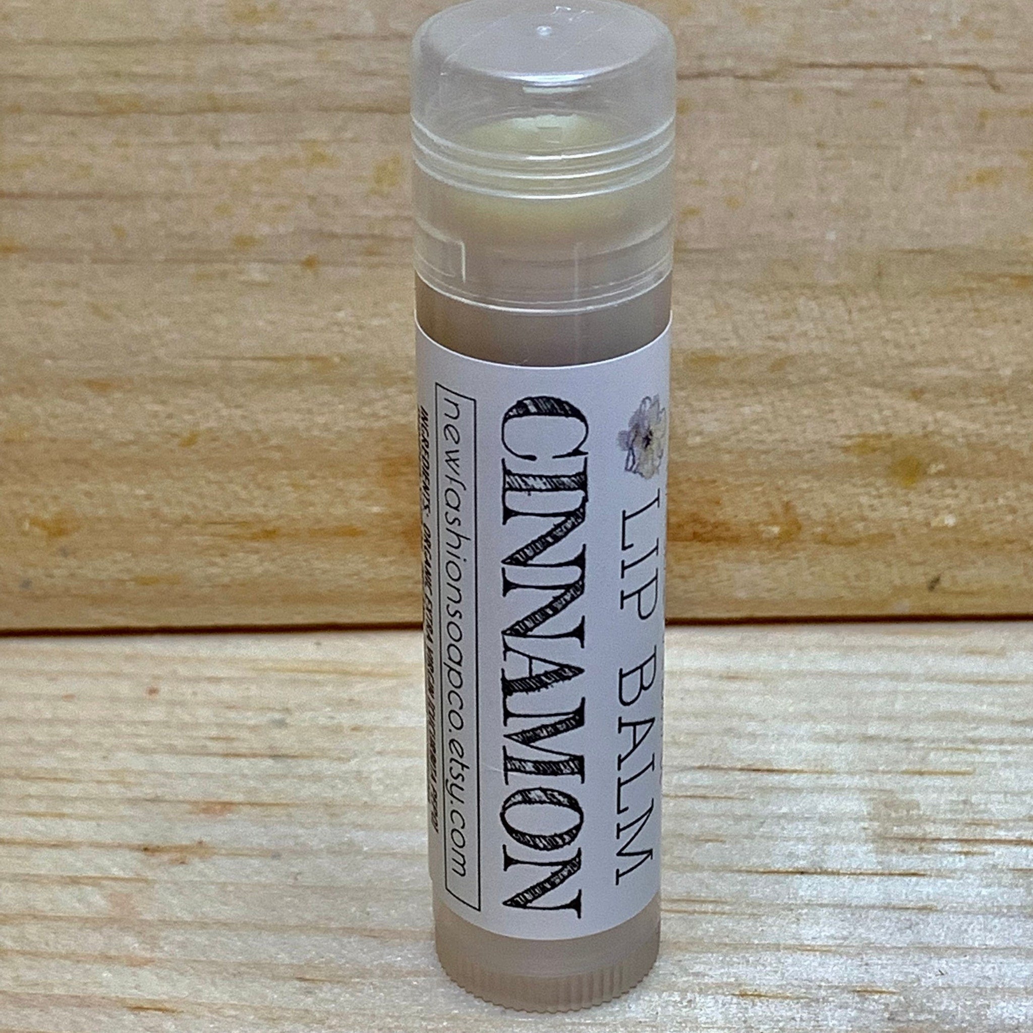 Lip balm tube with white label, cinnamon text, and clear cap on wood background