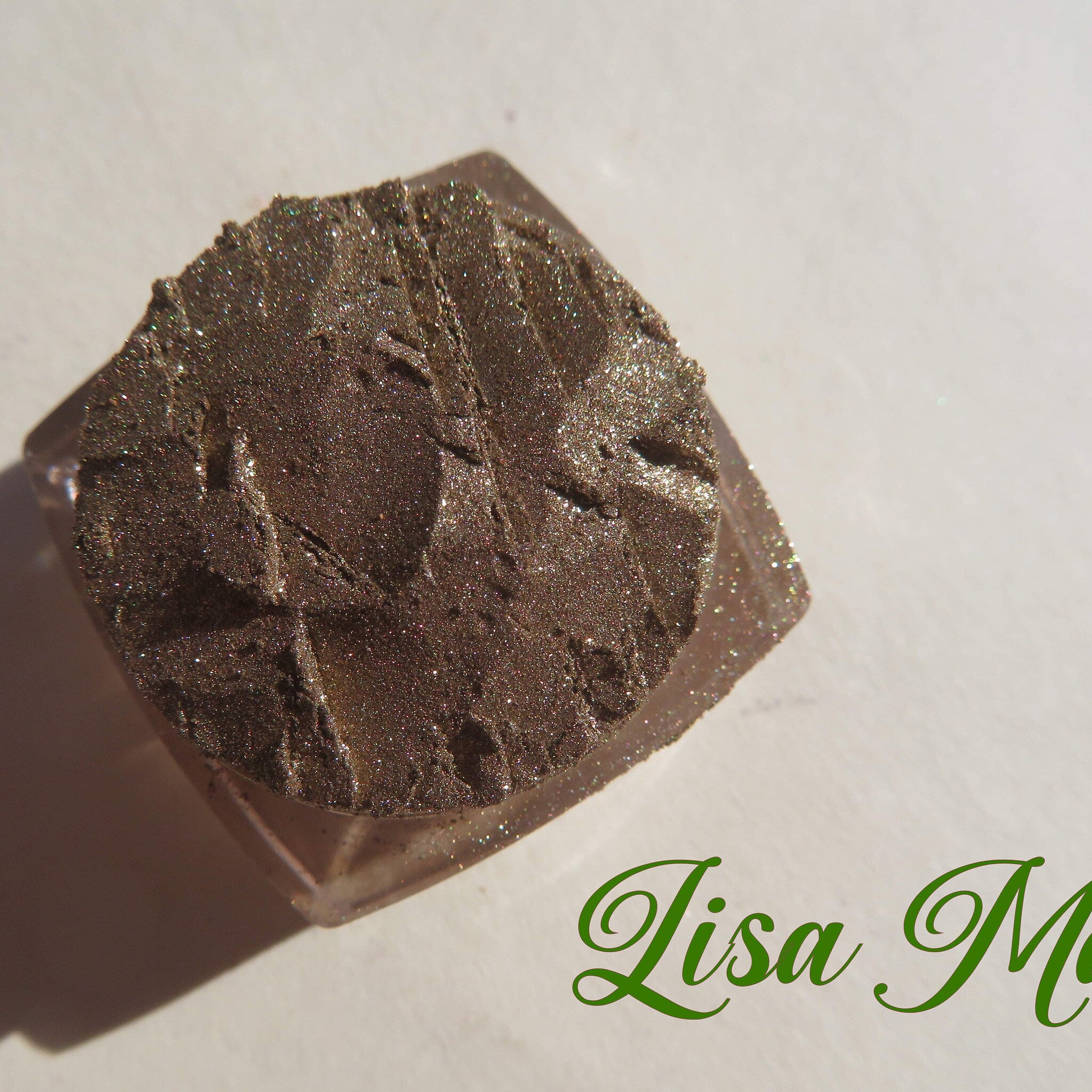 Eyeshadow pot with brown shimmery pigment and clear plastic container, Lisa M text visible
