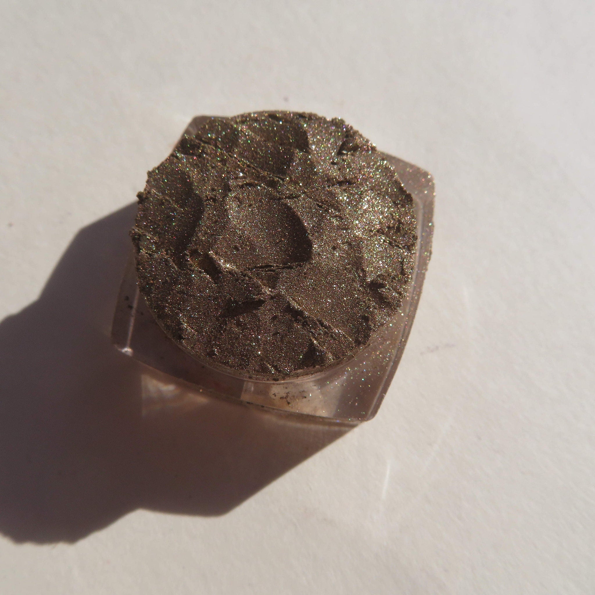 Eyeshadow, brown glittery powder in clear plastic container, textured surface