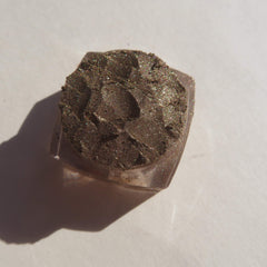 Eyeshadow, brown glittery powder in clear plastic container, textured surface