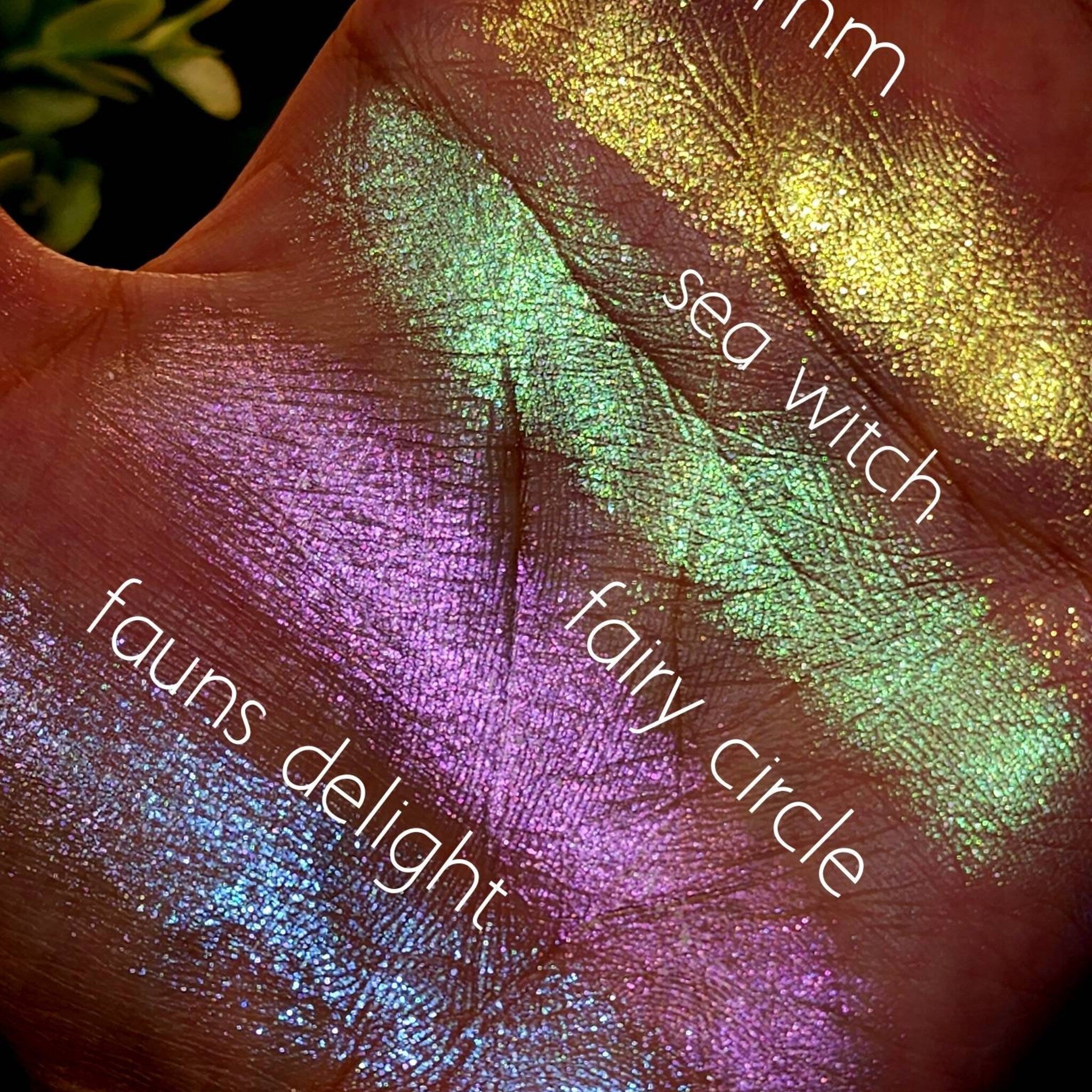 Close-up of fingers swatching iridescent green and pink duochrome eyeshadow with shimmer finish on skin