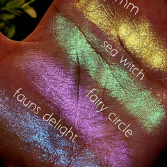 Close-up of fingers swatching iridescent green and pink duochrome eyeshadow with shimmer finish on skin