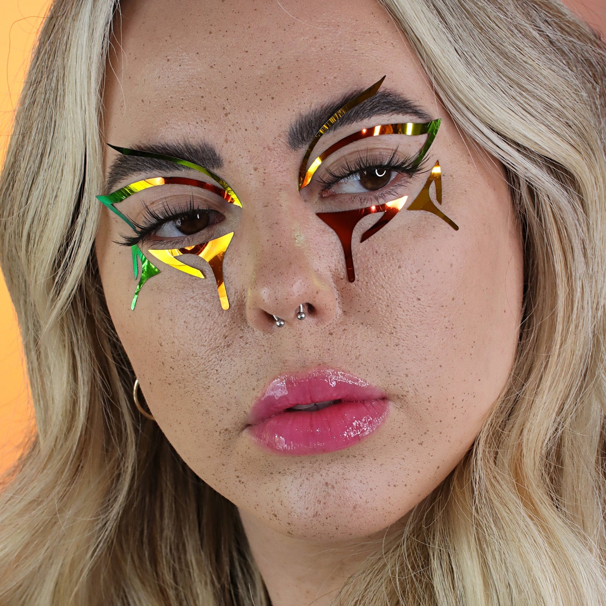 Eye makeup with iridescent foil, green and red accents, and geometric shapes on face
