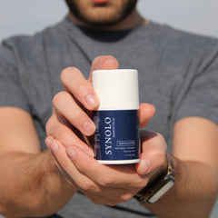 Facial Cleanser product, white and blue cylindrical container held in hands, Synolo Menceutical brand visible