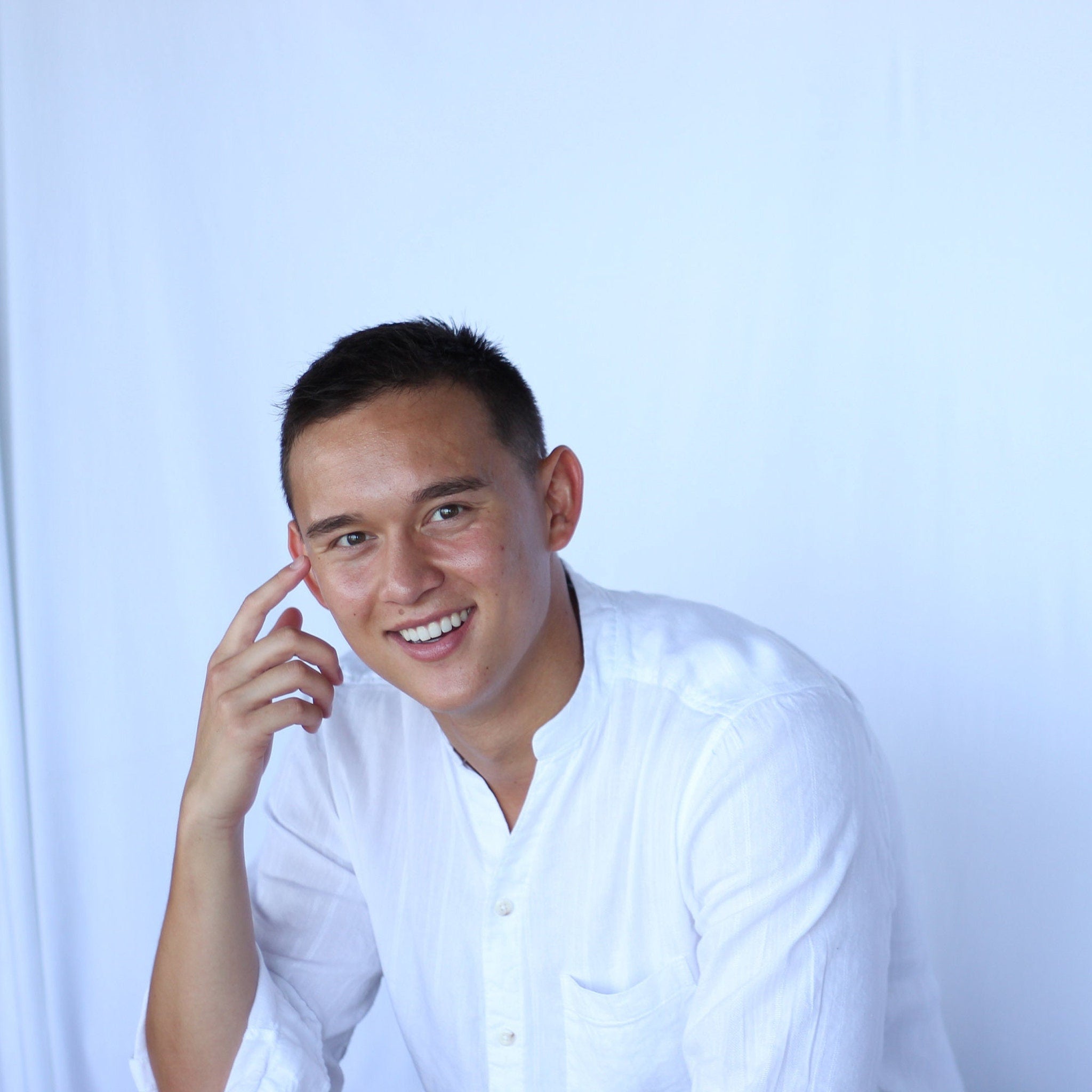 Smiling man wearing white collared shirt, touching face, with short dark hair and light skin