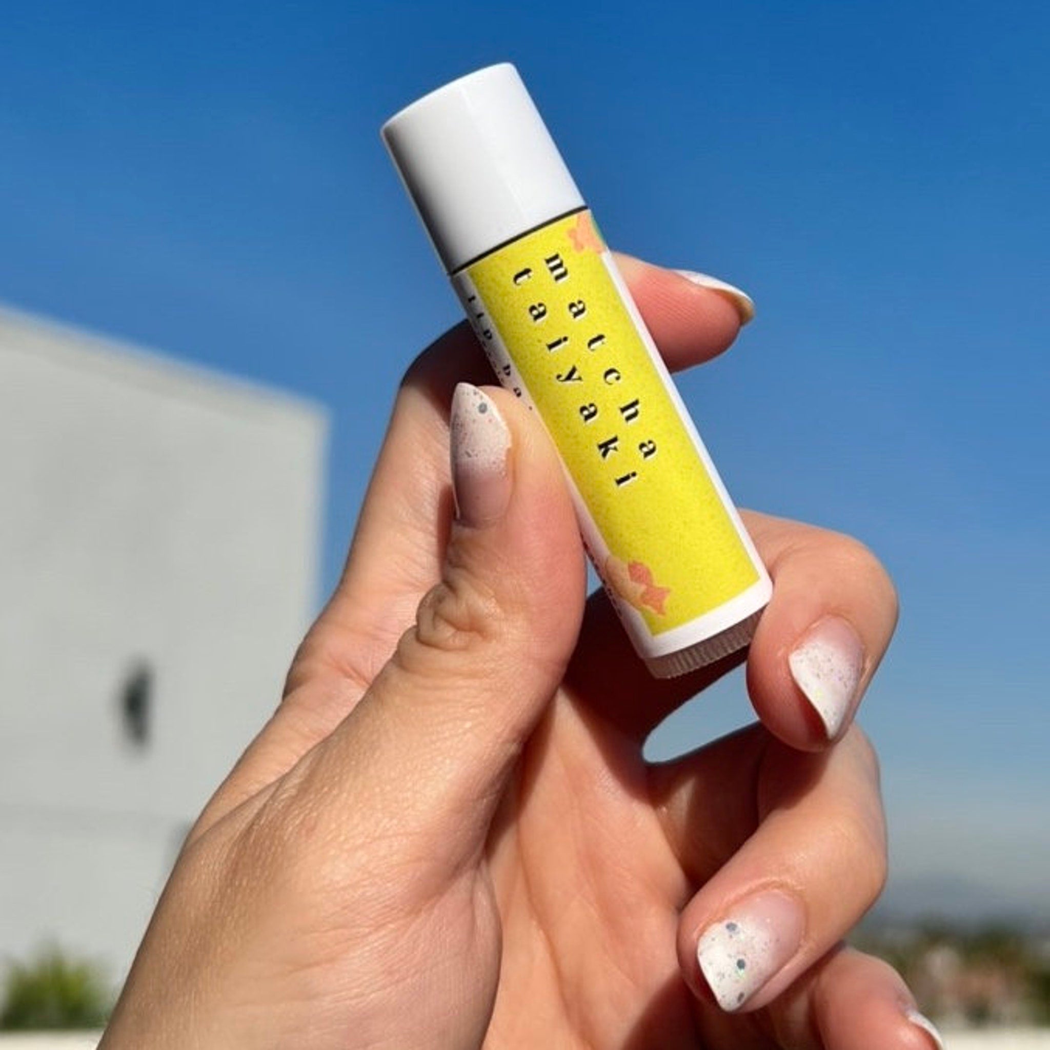 Lip balm tube with yellow label, white cap, and "matcha taiyaki" text held by hand