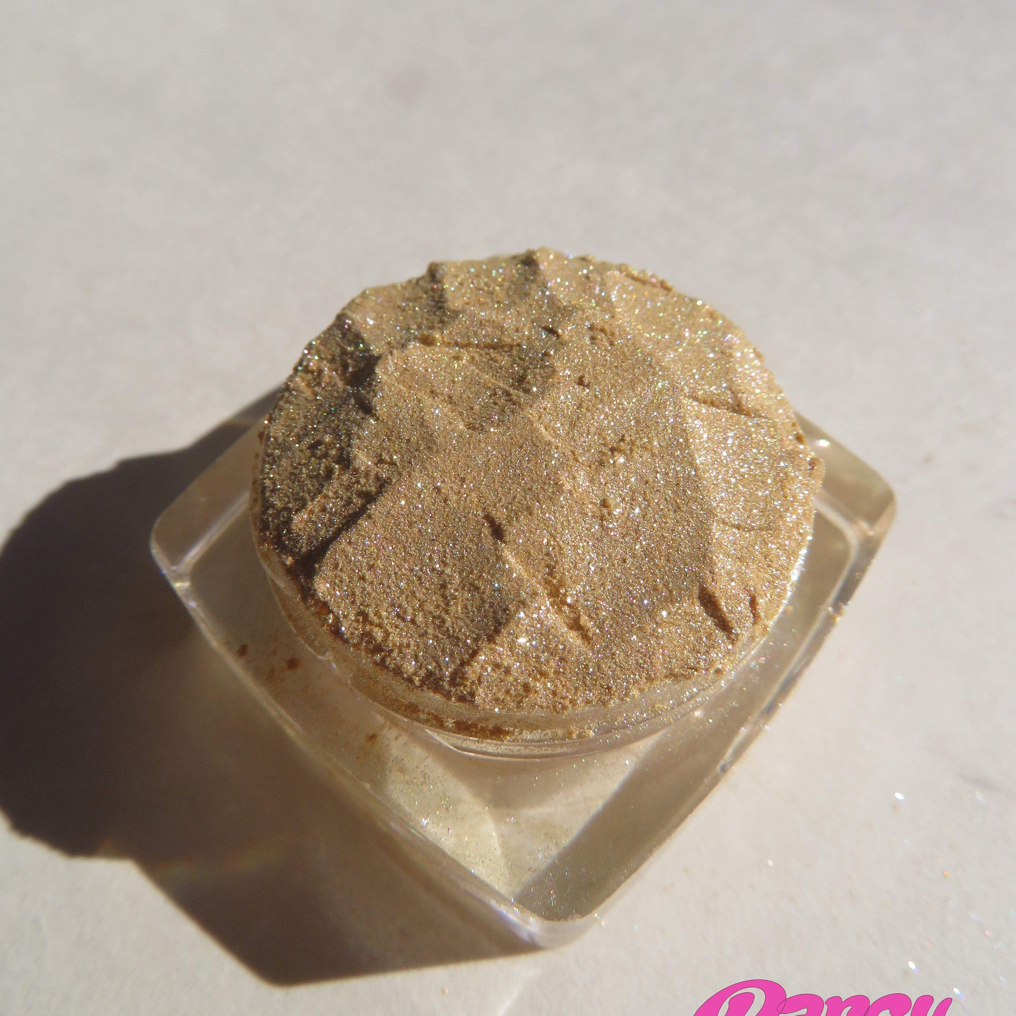 Eyeshadow compact with gold shimmer, faceted texture, and clear plastic container