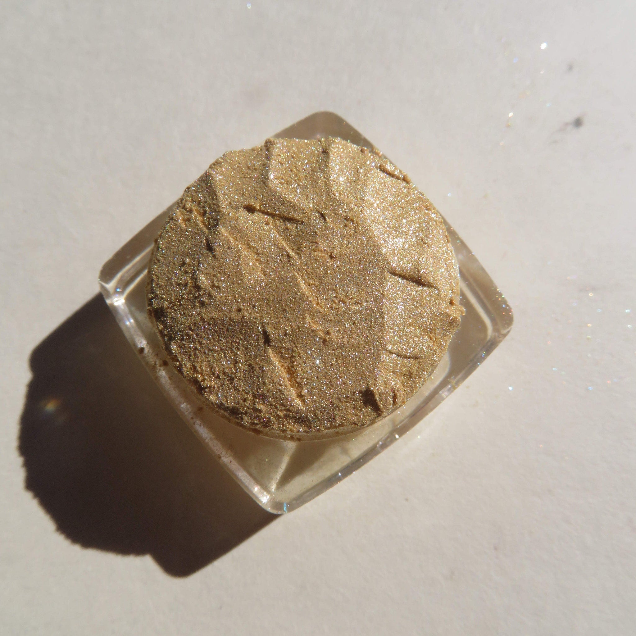 Glitter eyeshadow, gold shimmer, textured powder, clear square container