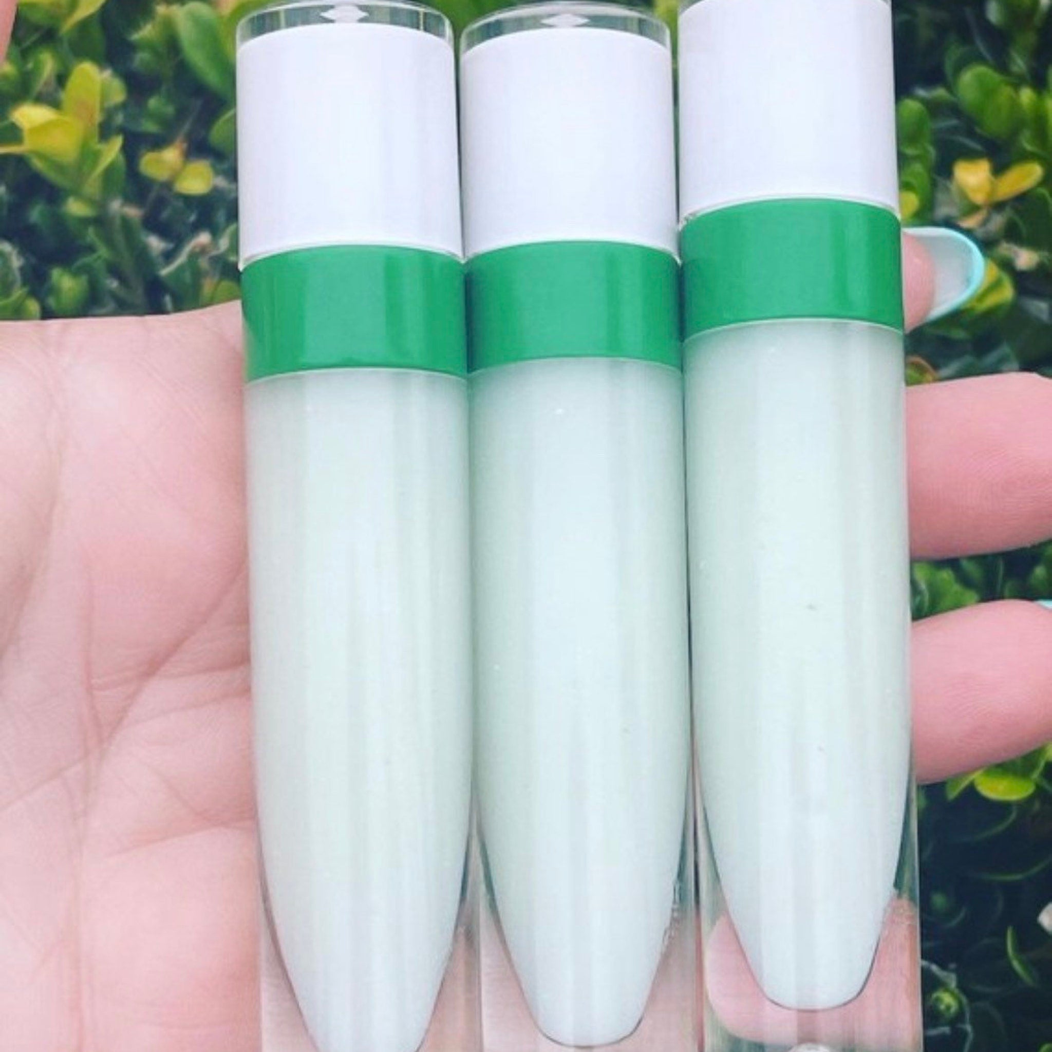 Lip gloss tubes with white and green accents, held in hand