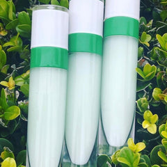 Lip gloss tubes with white, green, and clear glass, set against green foliage background